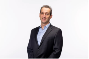 Man in a dark suit jacket and light blue shirt, affiliated faculty at the Institute of Bioinformatics, stands against a plain white background, smiling at the camera.