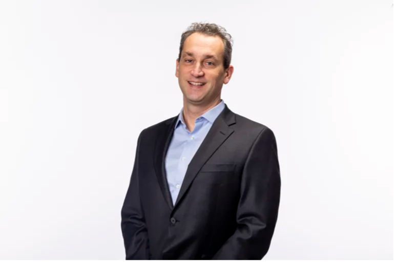 Man in a dark suit jacket and light blue shirt, affiliated faculty at the Institute of Bioinformatics, stands against a plain white background, smiling at the camera.