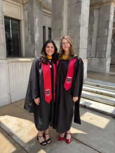 Two people in black graduation gowns and red stoles stand side by side, smiling outdoors in front of a stone building, celebrating their achievements in bioinformatics.